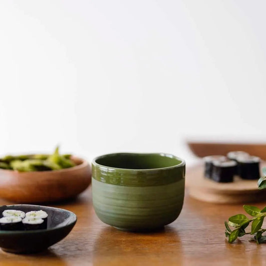 Eira Haul handmade ceramic matcha bowl in deep green with a matte exterior and glossy interior on a wooden table
