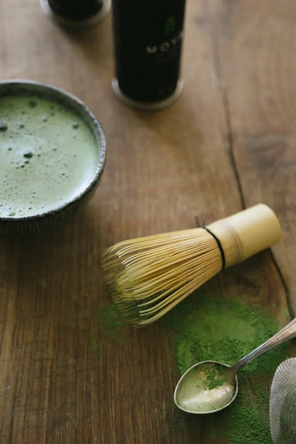 Traditional Japanese bamboo matcha whisk (chasen) on a table with matcha powder.