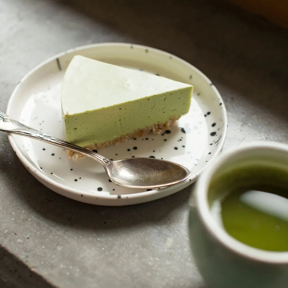 A plate with a slice of matcha cake next to a cup of tea.
