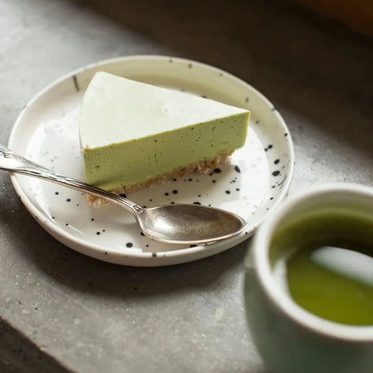 A plate with a slice of matcha cake next to a cup of tea.