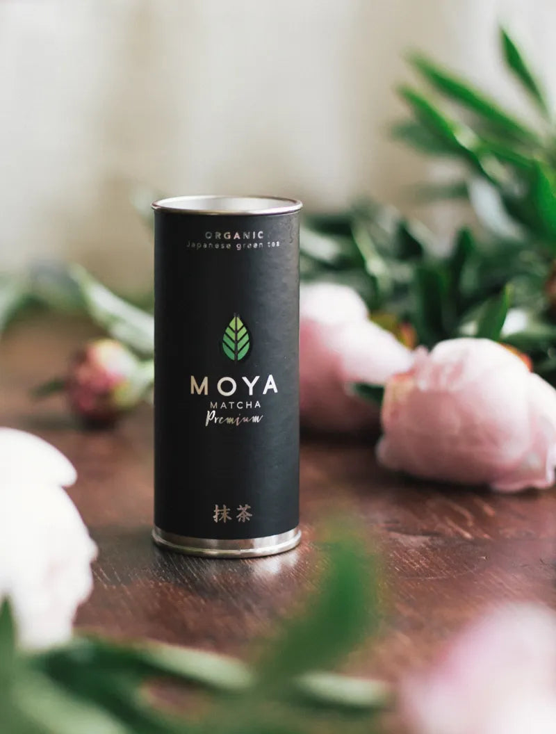Moya premium organic ceremonial matcha green tea in a 30 g package on a table with flowers.