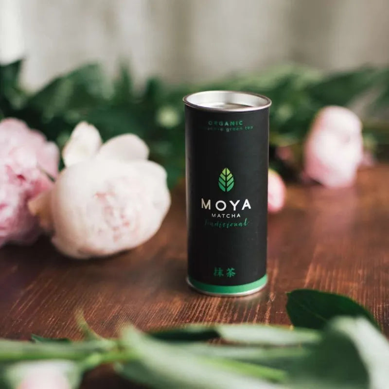 Moya traditional organic matcha green tea in a 30 g package on a table with flowers.