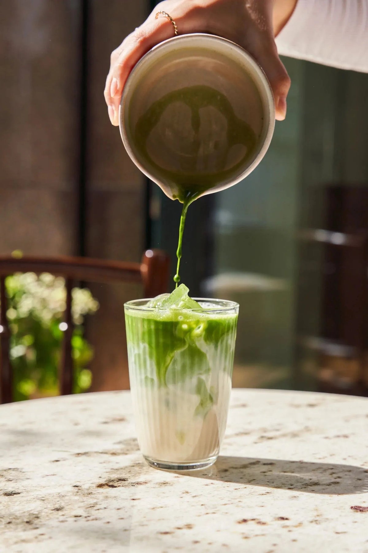 Pouring whisked matcha into a glass of milk to make a matcha latte.
