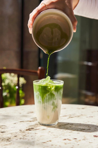 Pouring whisked matcha into a glass of milk to make a matcha latte.