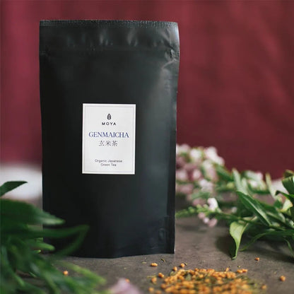 Moya organic Japanese genmaicha green tea with roasted rice with bag package on a table with flowers.