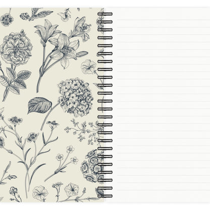 A spiral-bound lined notebook shown open, with a cream cover decorated in black floral line art and blank lined pages visible on the right.