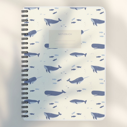 Eira Haul A5 notepad with a cream background and blue whale and narwhal pattern, featuring black wire comb binding.