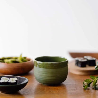 Eira Haul handmade ceramic matcha bowl in deep green with a matte exterior and glossy interior on a wooden table