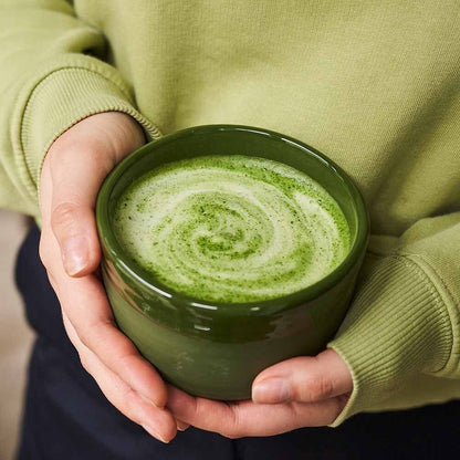 Eira Haul handmade ceramic Midorinami matcha bowl in deep green held in hands with freshly whisked frothy matcha tea