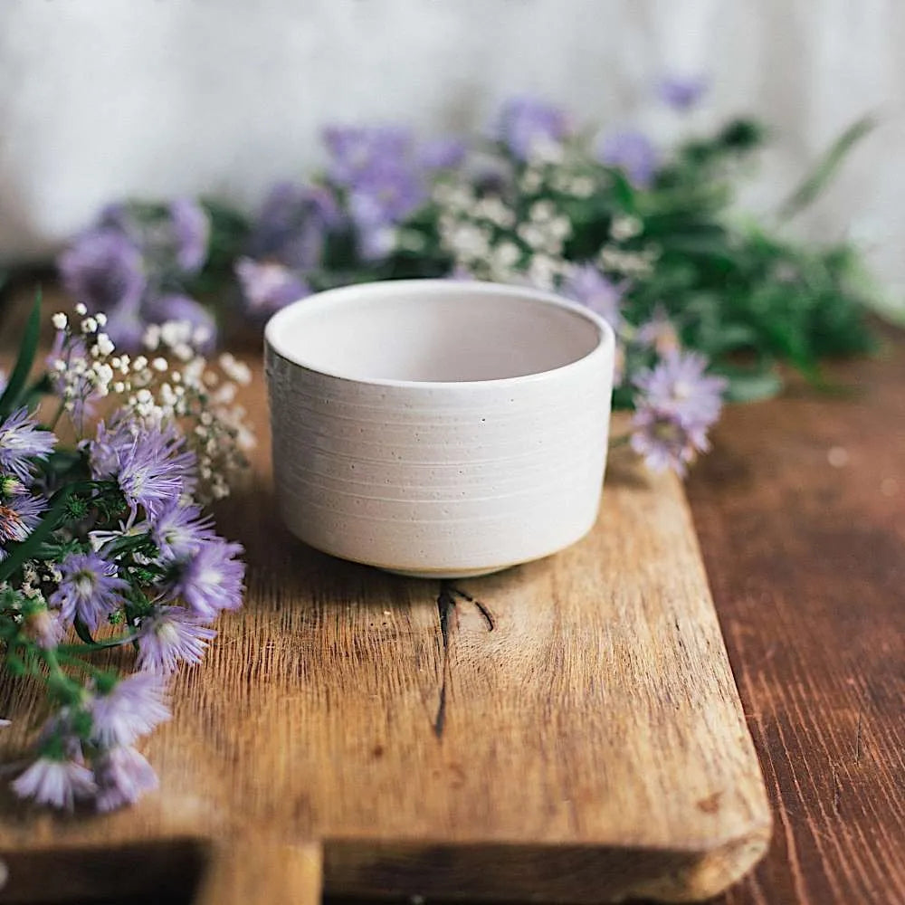 Eira Haul handmade ceramic matchawan fuyumoya bowl in white on a wooden board with purple flowers