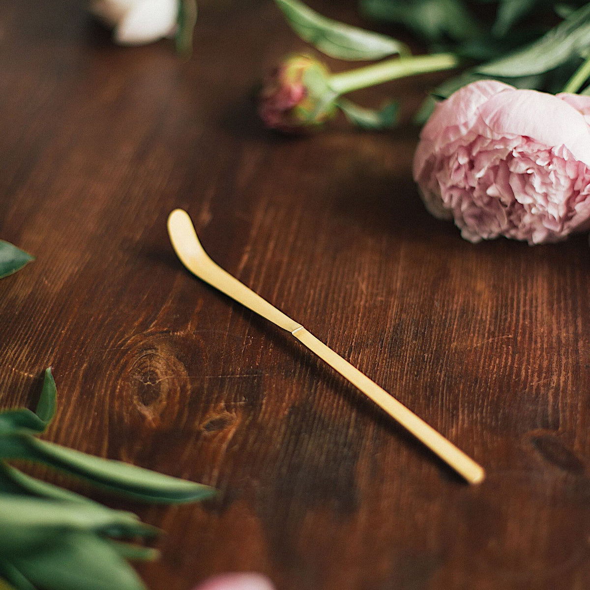 Traditional Japanese matcha bamboo spoon (chasaku) on a wooden table with flowers.