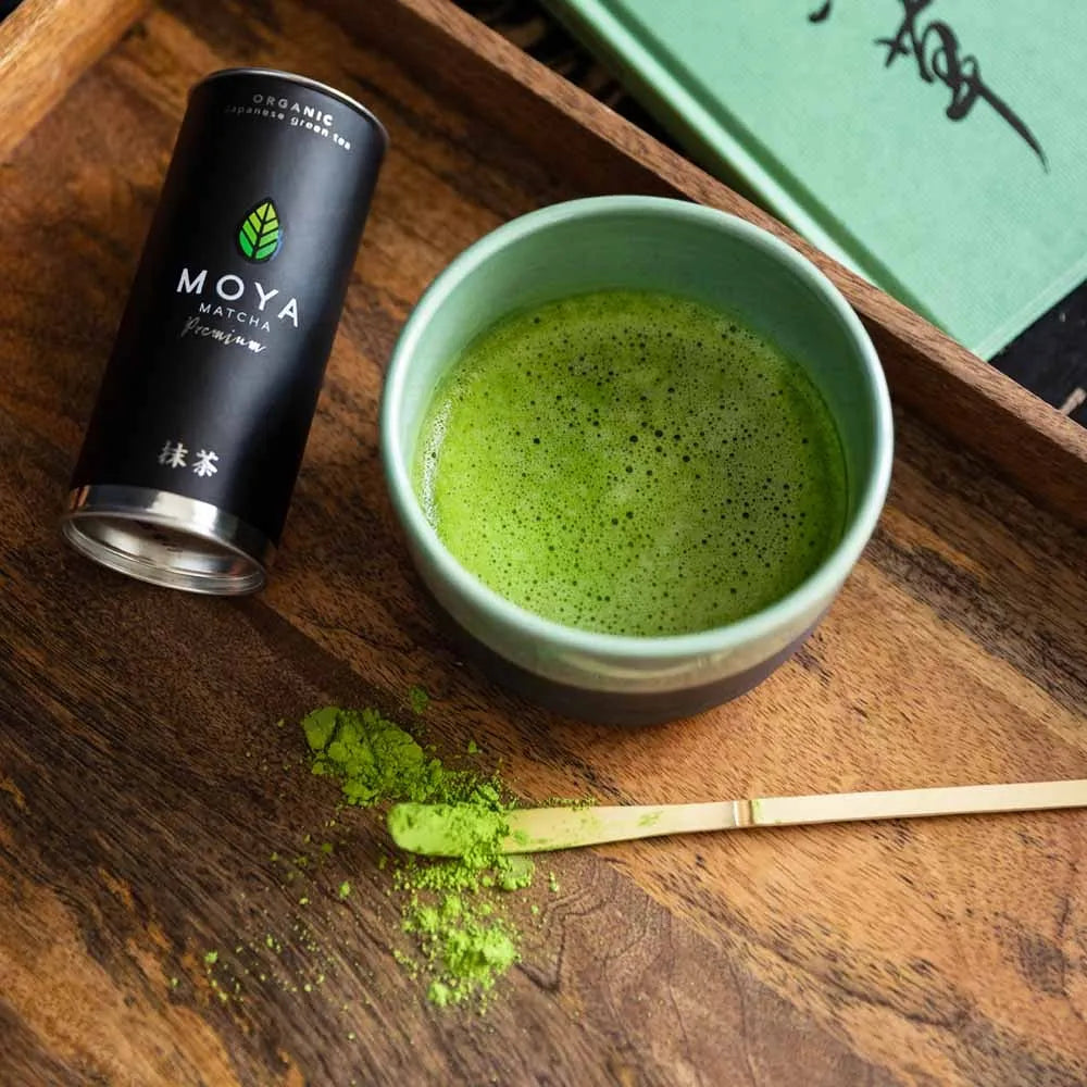 Traditional Japanese matcha bamboo spoon (chasaku) on a wooden table with matcha bowl and matcha powder.